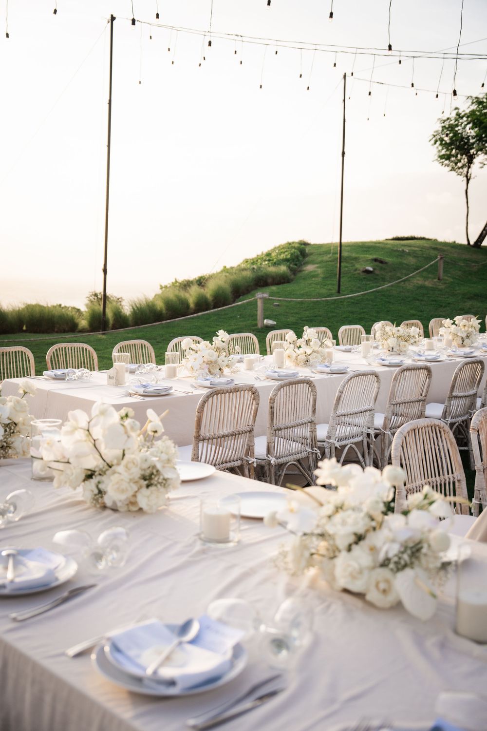 Elegant outdoor wedding reception table with white floral centerpieces and place settings stretching into the distance.
