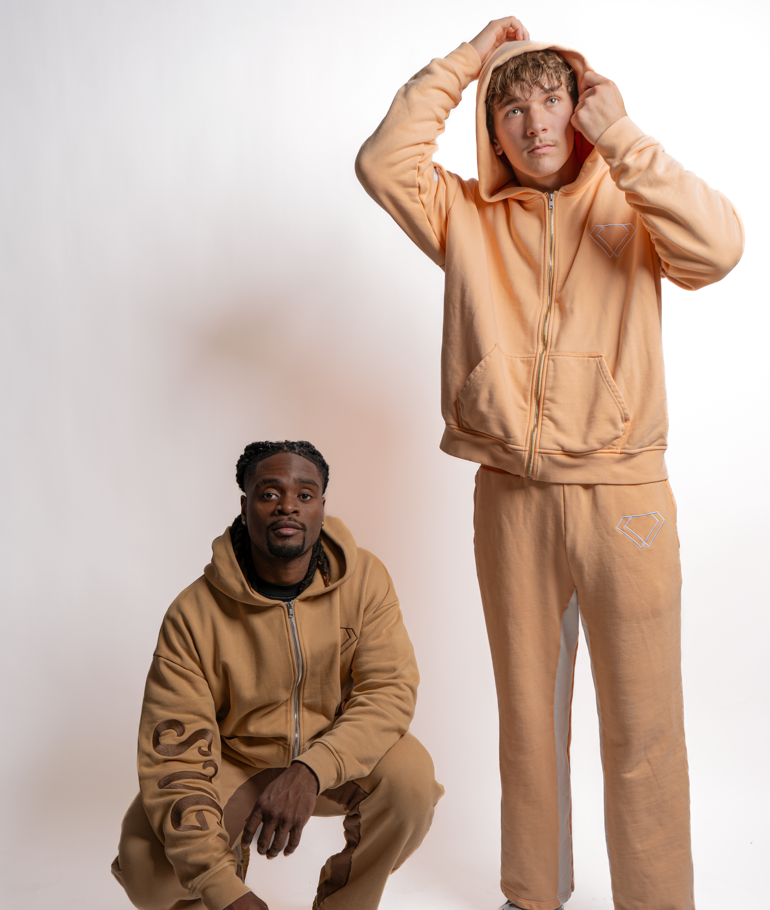 Two people wearing matching beige hooded sweatsuit sets pose against a white background.