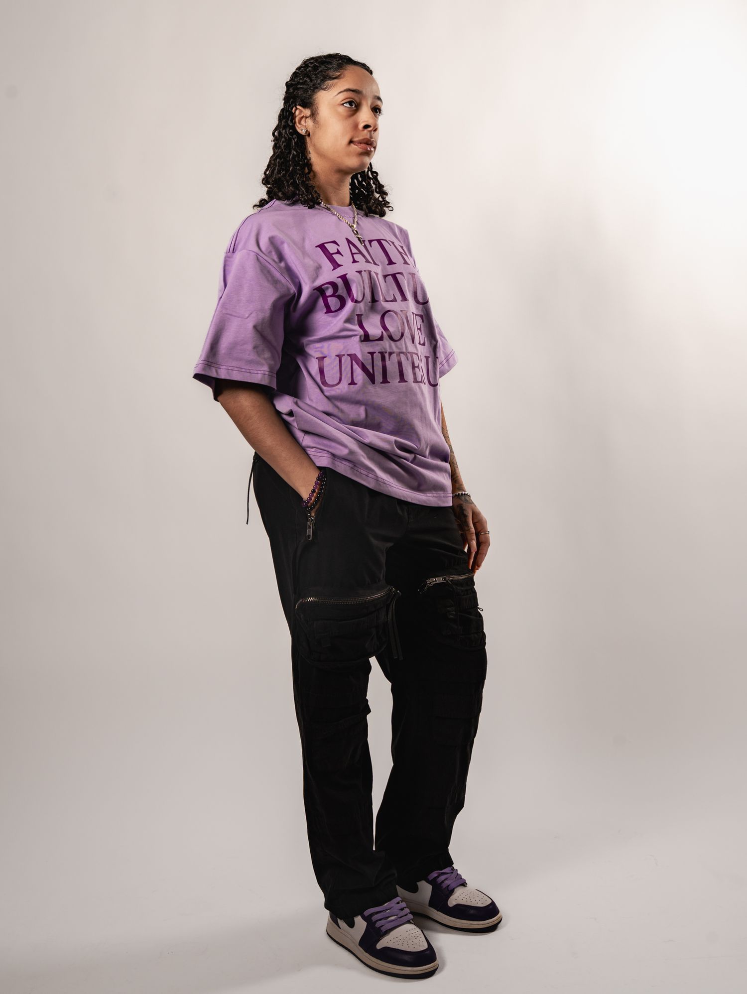 Model wearing a purple t-shirt and black pants poses in different angles against a white studio backdrop.