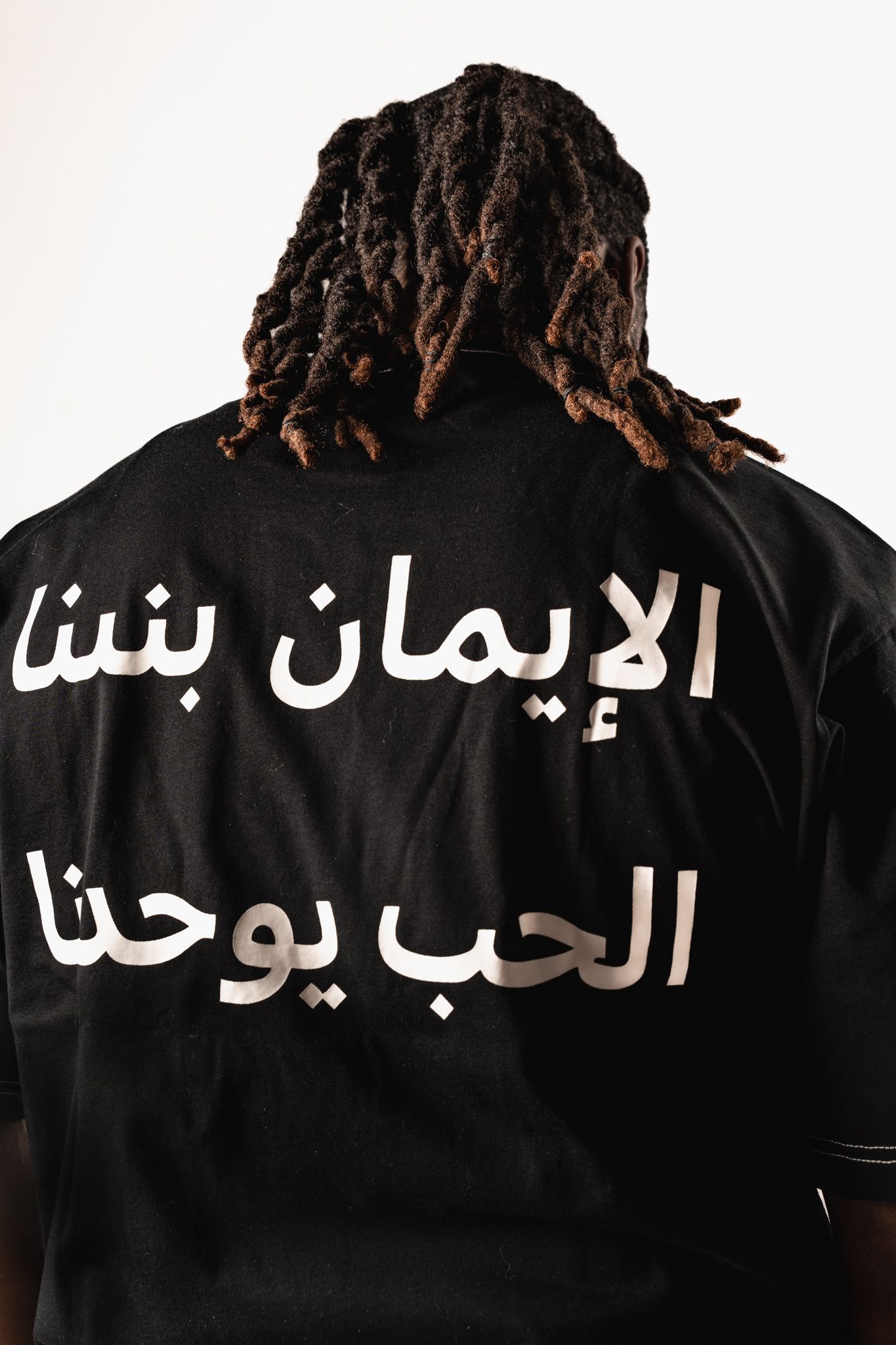 Back view of black t-shirt with Arabic text design against white background.