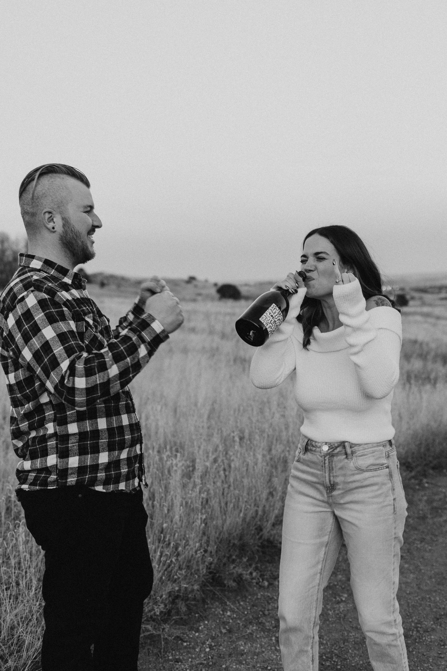 Black and white photo of two people drinking from bottles in an outdoor field with tall grass.