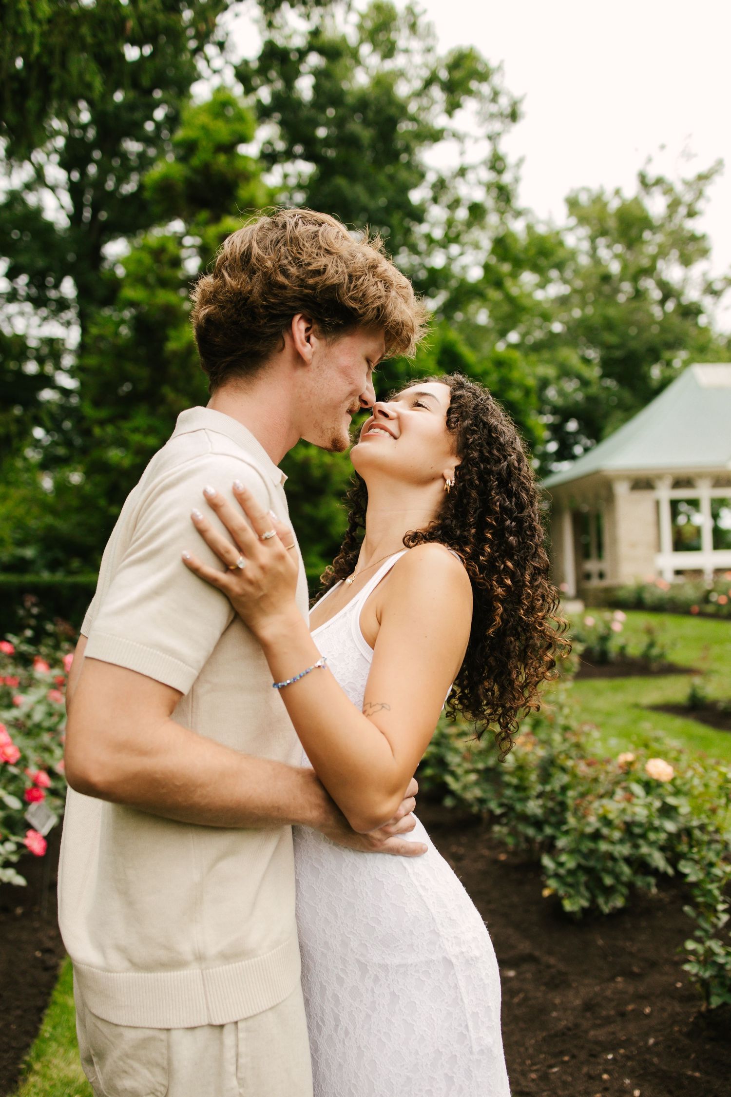 Couple shares intimate dance moment in garden setting wearing matching light outfits.