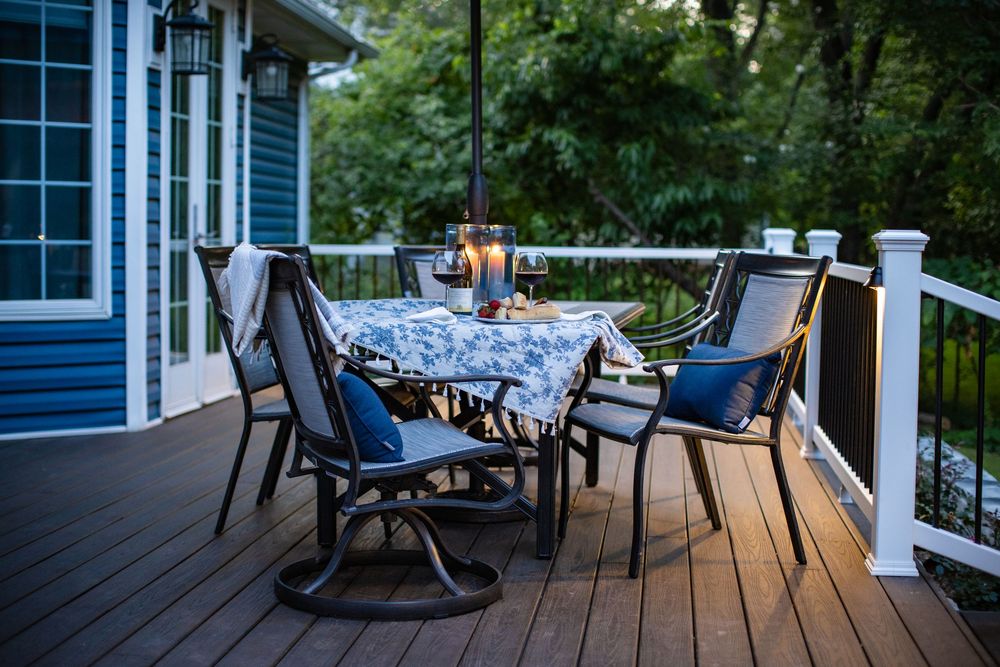 Cozy outdoor deck setting with patio furniture, blue cushions, and candlelight at dusk beside a blue house.