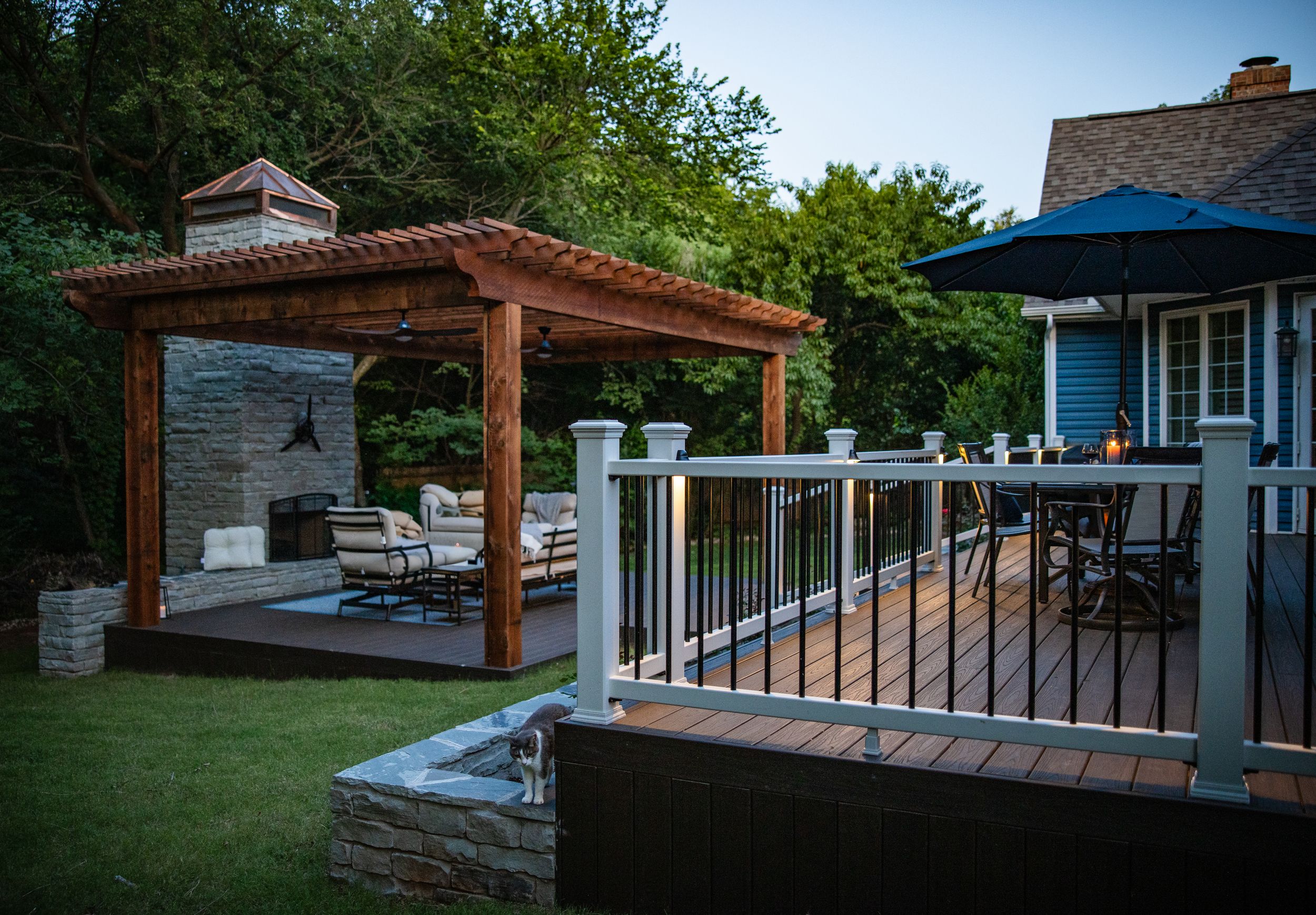 Beautiful backyard deck with wooden pergola featuring comfortable seating and modern white railings at dusk.