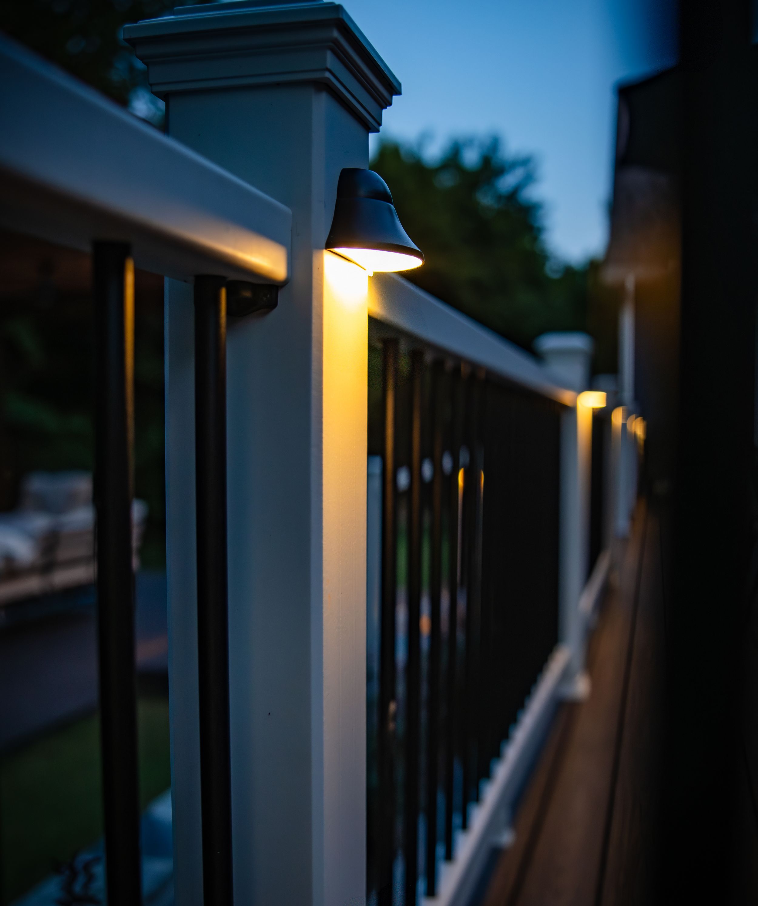 Close-up view of white porch railing posts at dusk with warm exterior lighting creating a cozy ambiance.