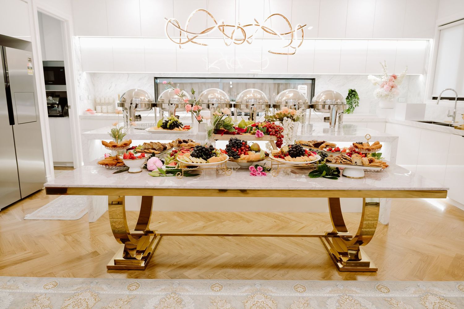 A minimalist white and gold event venue with a long banquet table decorated with light pink floral arrangements.