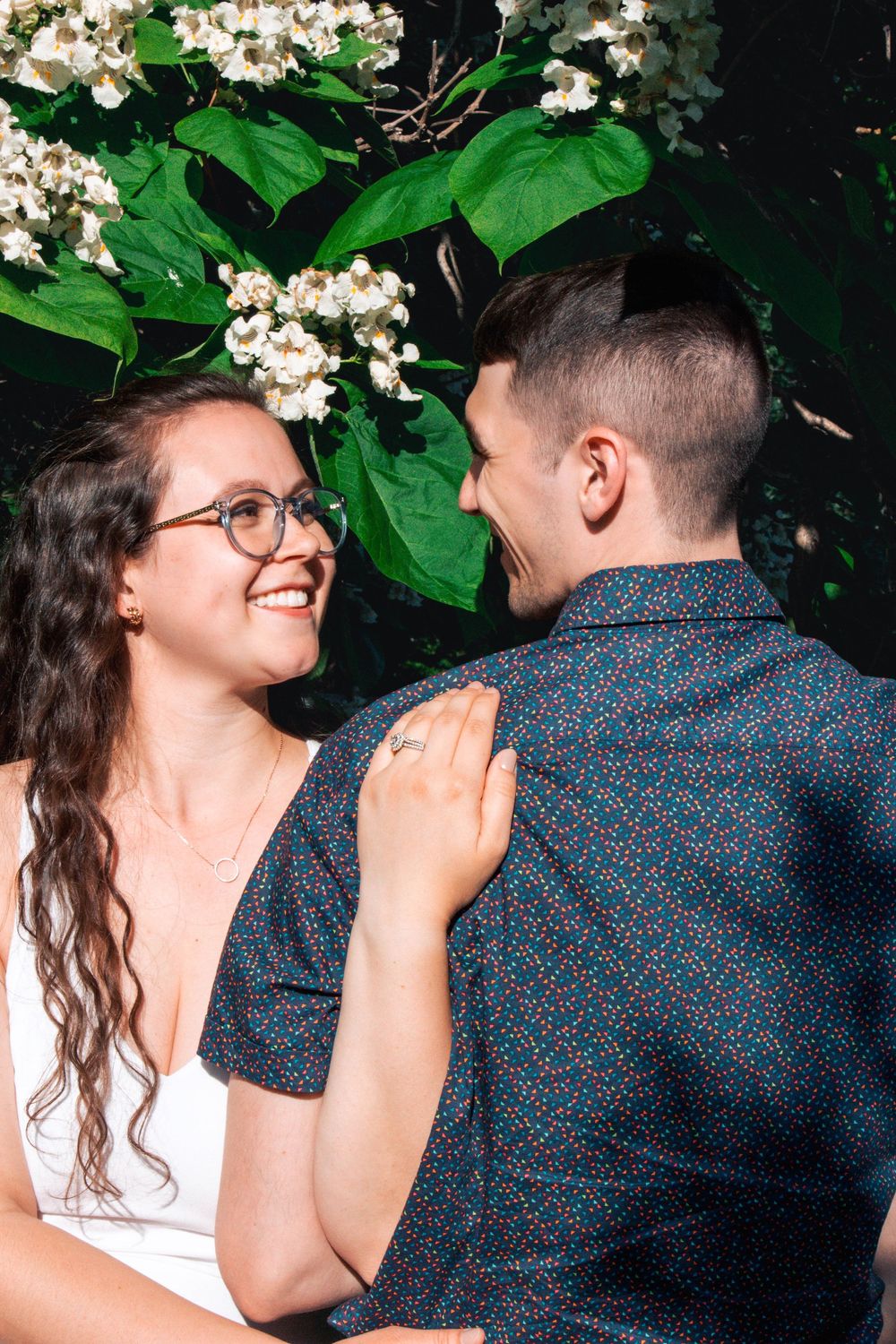 A romantic moment captured in a garden with white flowers and lush green foliage in the background.