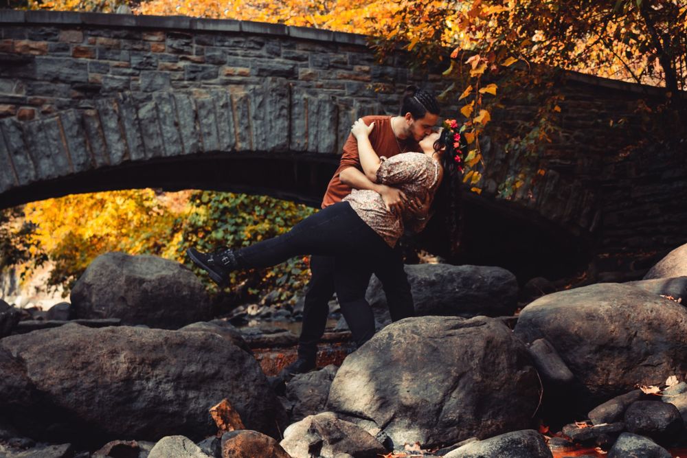 A romantic couple relaxes on large rocks by a creek during golden hour sunset lighting.