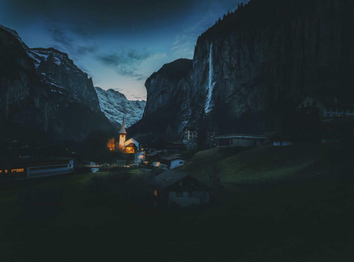 Mountain peaks rise dramatically against a moody blue twilight sky in Lauterbrunnen Valley, Switzerland.