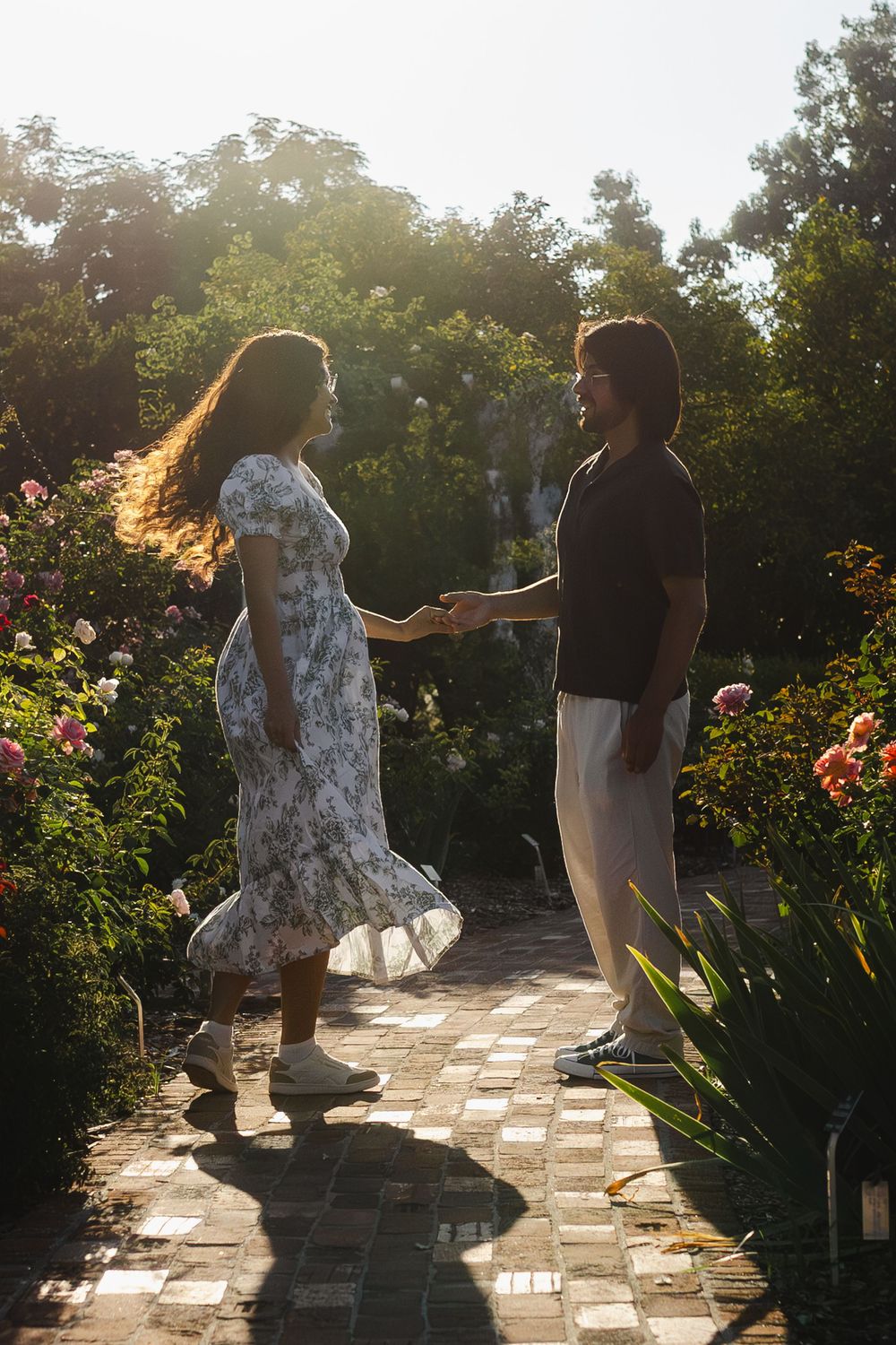 Two people dancing on a stone pathway surrounded by lush garden foliage at sunset.