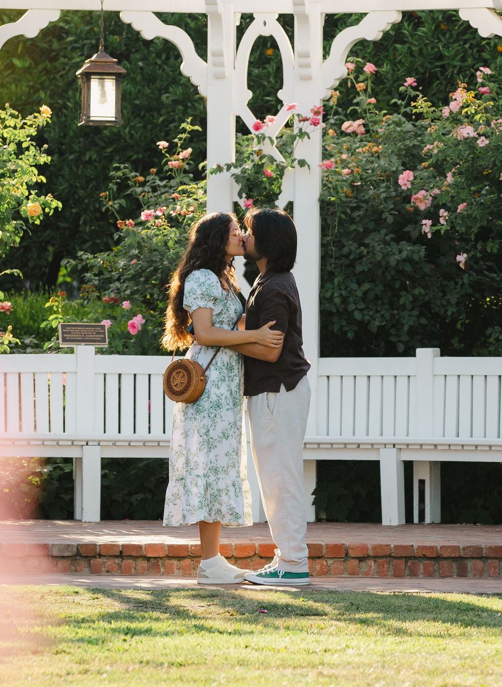 A romantic moment captured under a white garden gazebo surrounded by blooming roses.