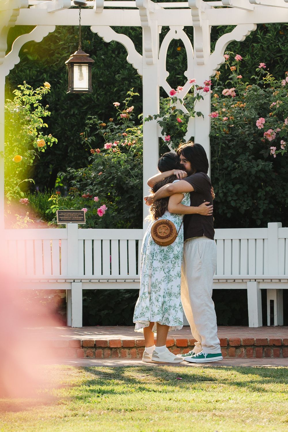 Sweet candid moments unfold beneath a white pergola in a lush garden setting.