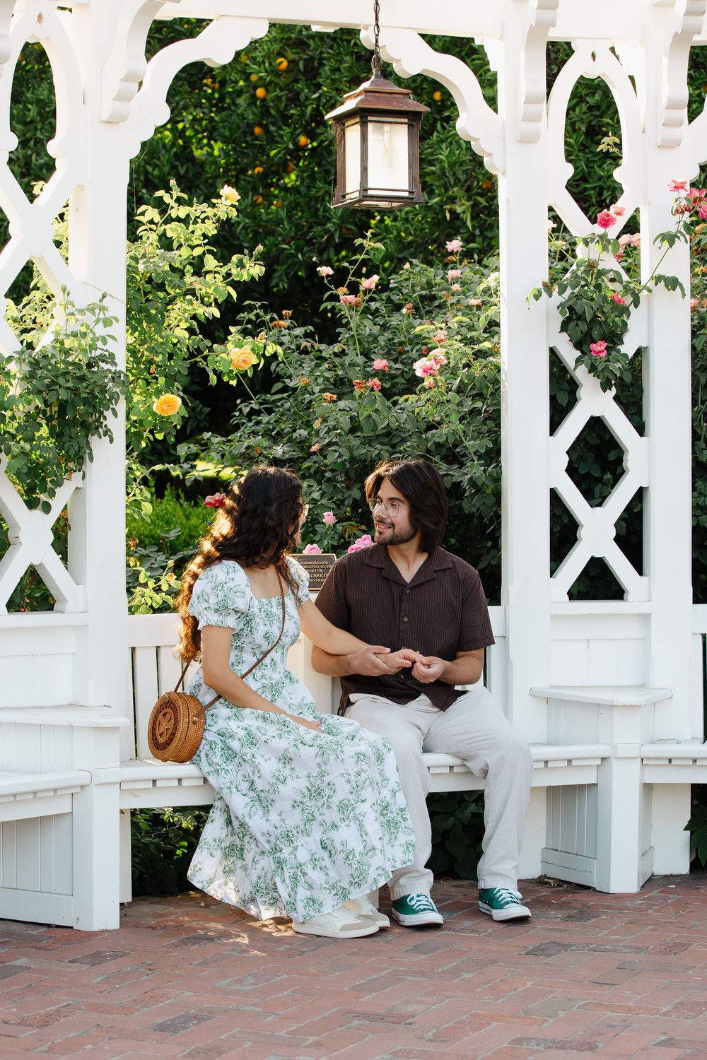 A couple shares intimate moments on a bench beneath an ornate white gazebo.
