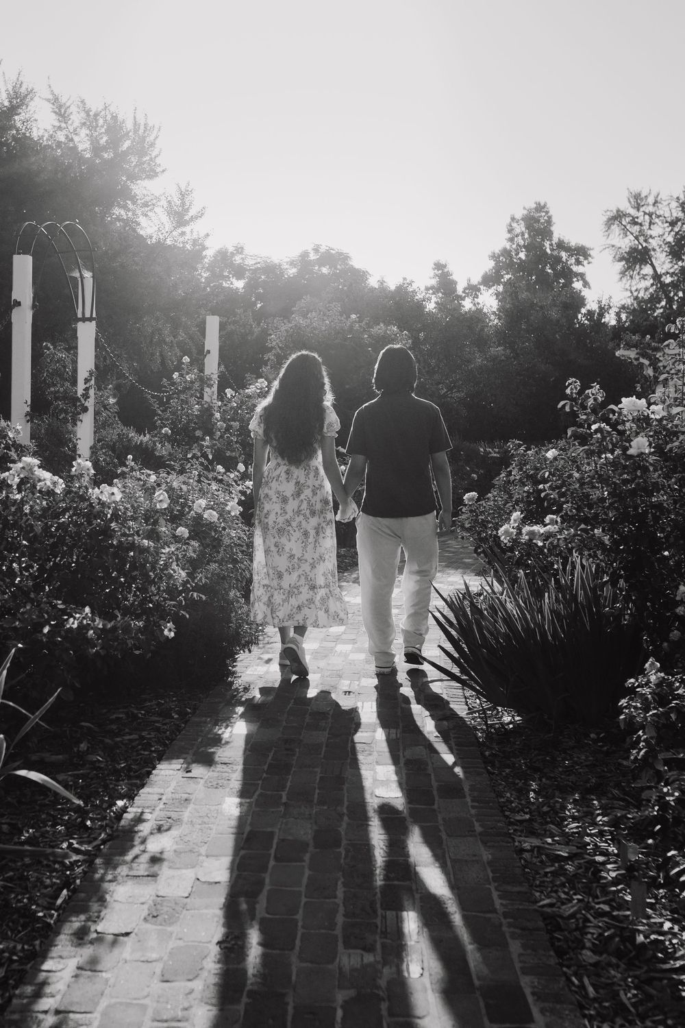 Silhouette of a couple walking down a garden path surrounded by flowers at sunset.