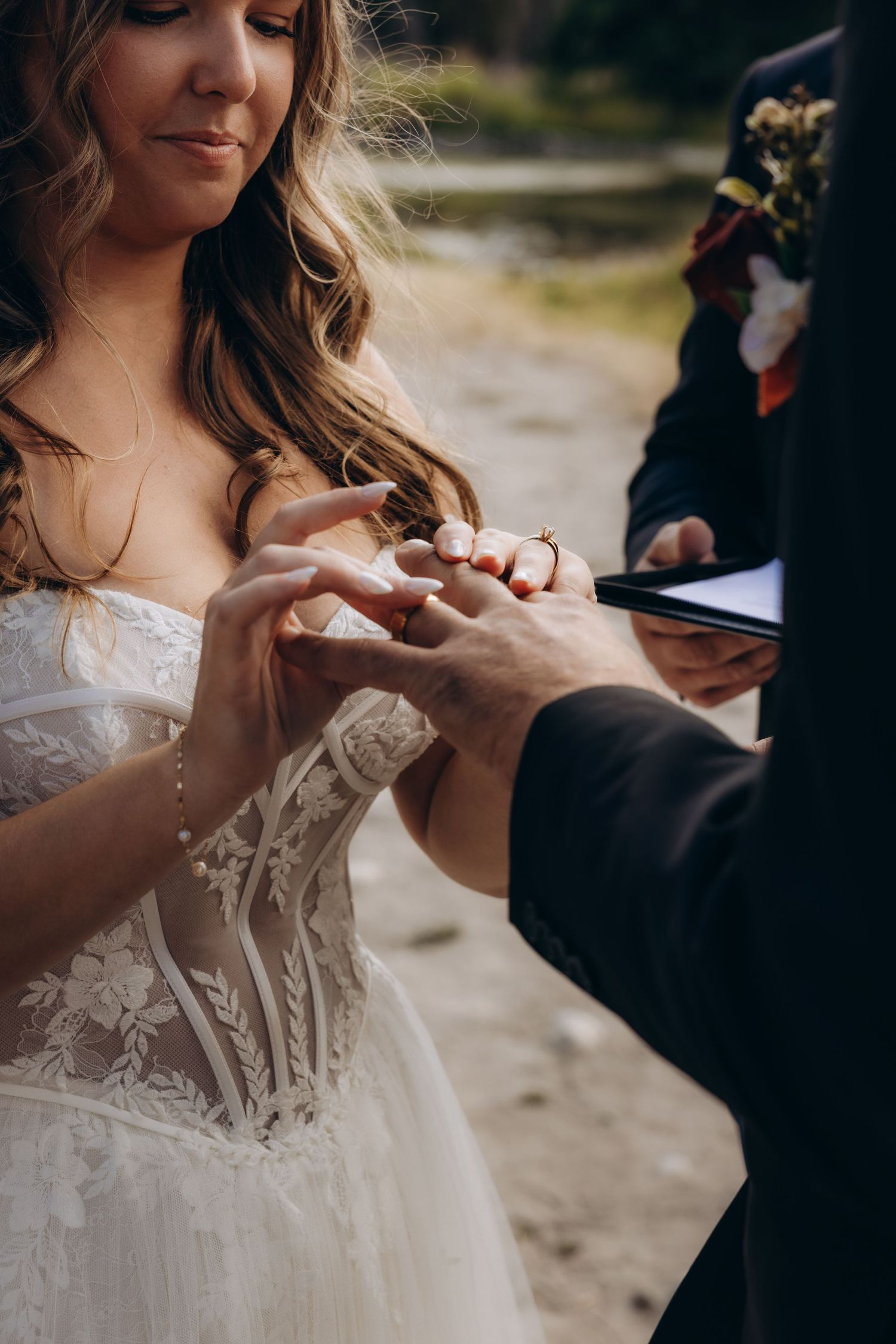 Close-up details of a delicate white lace wedding dress being fastened or adjusted.