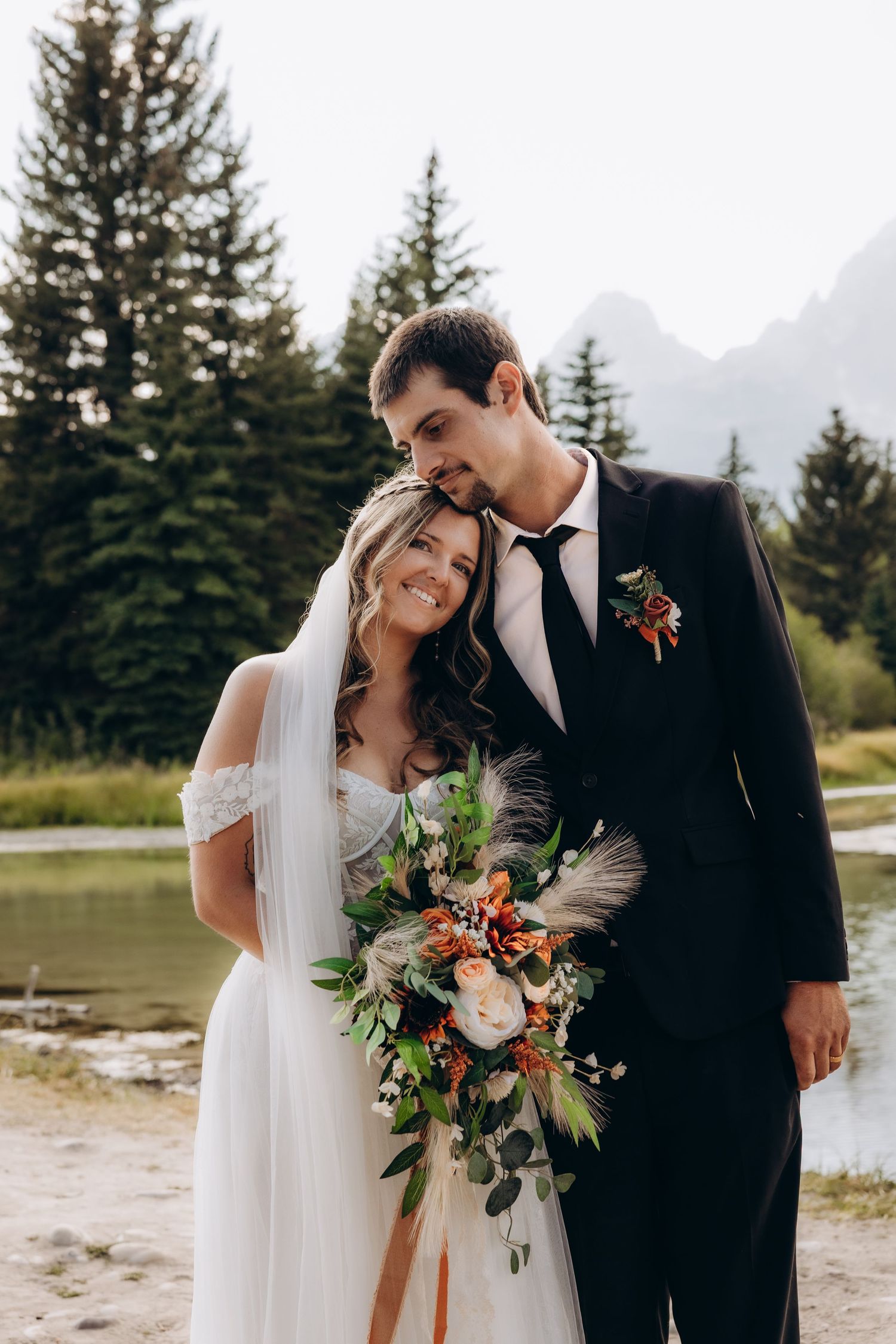 Romantic wedding portrait in front of pine trees and mountains with autumn bouquet of flowers and pampas grass.
