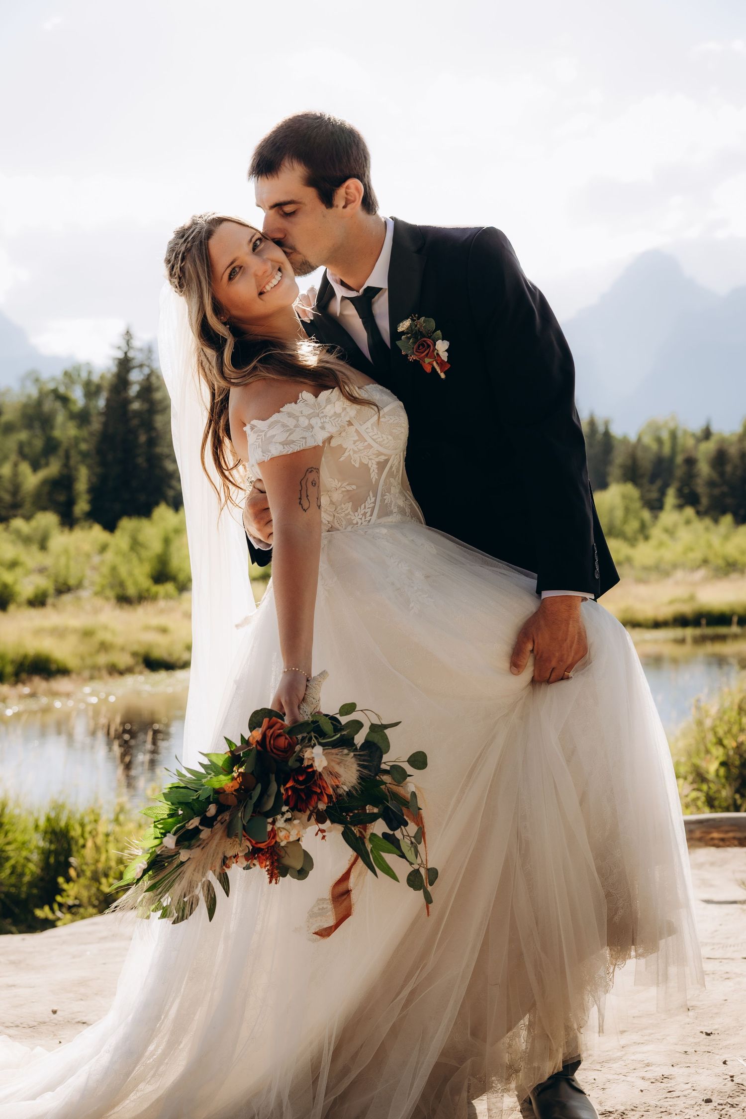 A romantic wedding photoshoot showing tender moments between a couple by a lake in nature.
