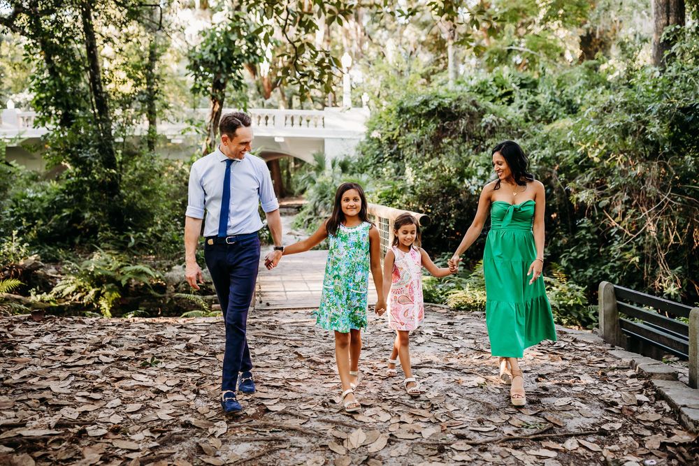 A family walks together holding hands along a shaded stone pathway in coordinated green and blue outfits.