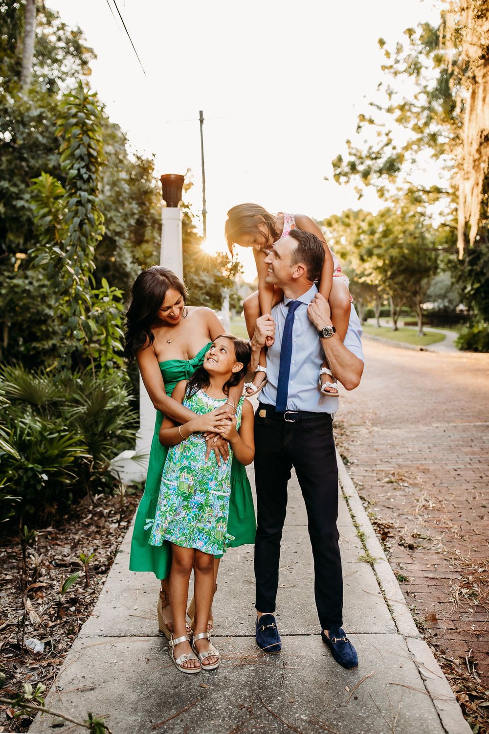 A family enjoying a candid moment together on a sunset-lit sidewalk while dressed in formal attire.