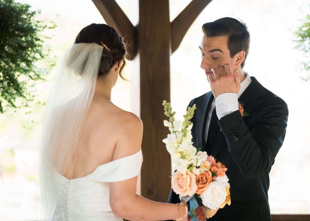 Emotional first look sequence between couple in formal wedding attire under rustic wooden structure.