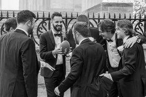 Black and white photo of groomsmen laughing and celebrating together outside a church on a wedding day.
