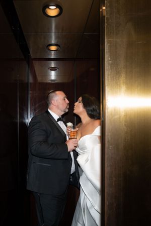 Bride and groom sharing a romantic moment in elevator, groom holding cocktail.