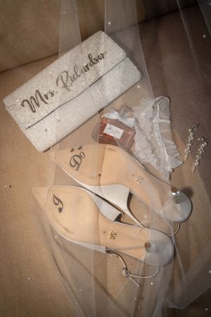 Bridal accessories flat lay featuring Mrs. Richardson clutch, clear heels, garter, perfume, and veil.