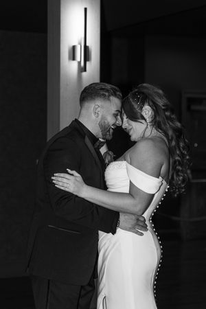 Black and white photo of a smiling bride and groom sharing an intimate moment during their first dance at wedding reception.