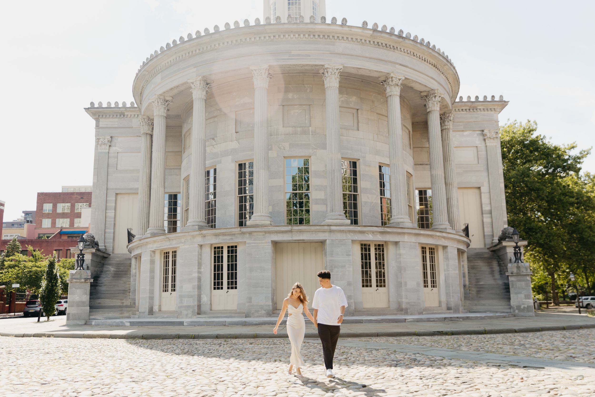Couple walking in front of a grand neoclassical building with white columns and dome architecture.