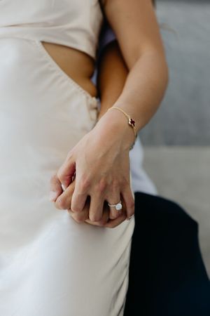 Close-up of a delicate bracelet and engagement ring on a person wearing a white dress.
