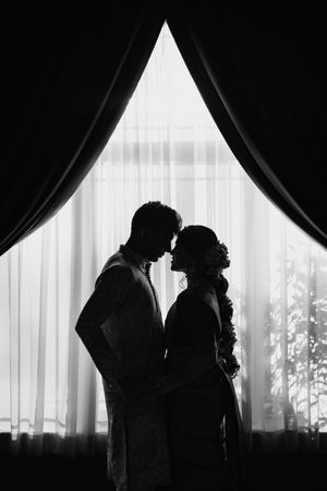 Silhouette of a romantic couple standing by a window with flowing curtains.