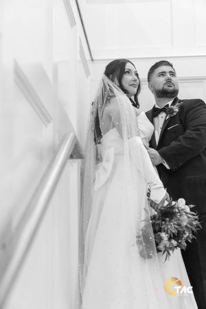 Black and white photo of a bride in a veil holding a bouquet and groom in a tuxedo looking up at their wedding.