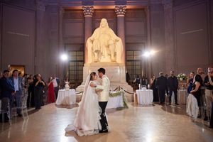 Couple dancing at elegant indoor venue with large statue and columns in background.