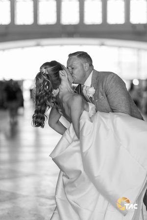 Black and white wedding photo of bride and groom sharing a romantic dip kiss inside an elegant venue.