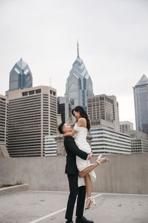 Couple embracing in front of Philadelphia skyline with iconic skyscrapers in background.