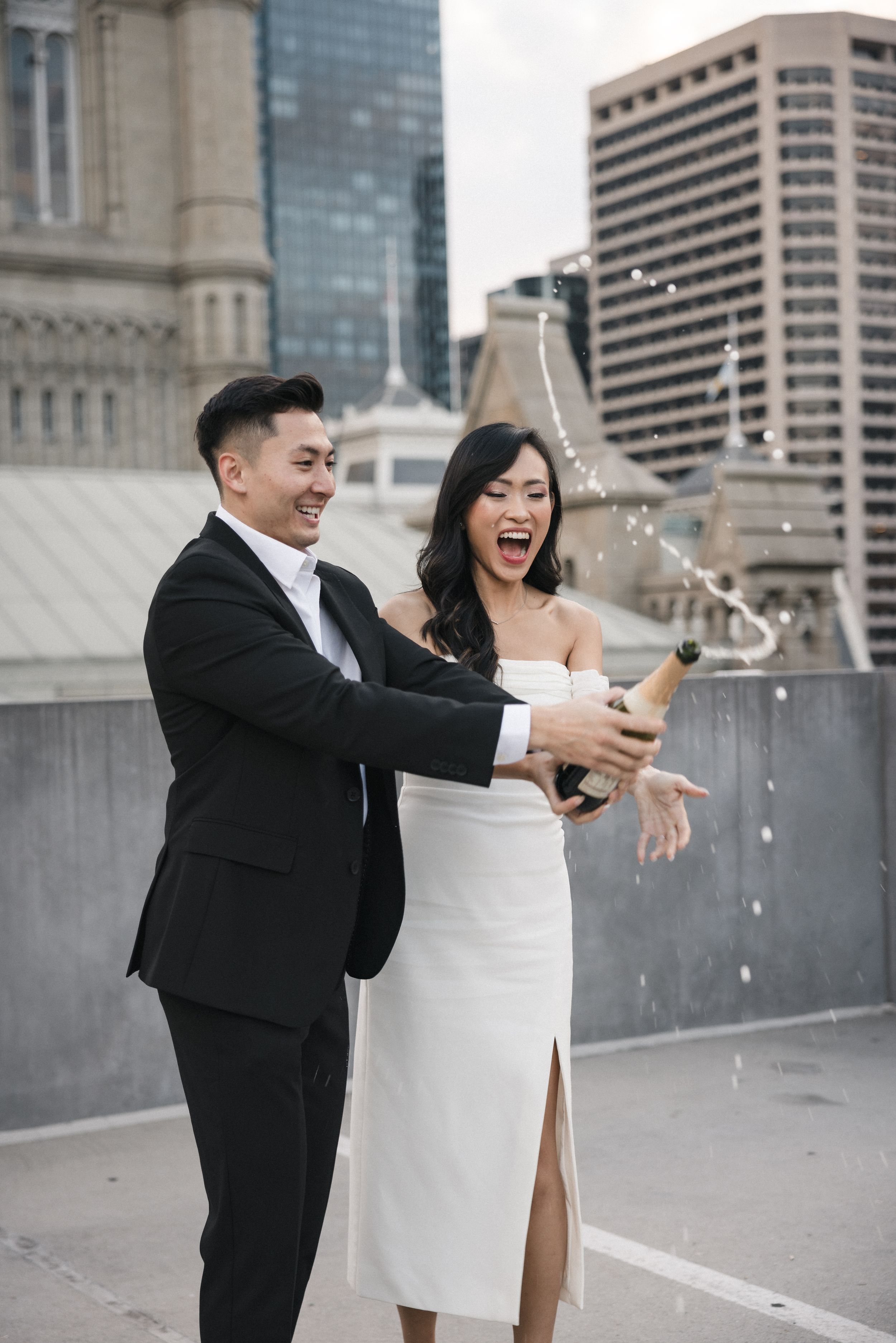 Couple celebrating with champagne on rooftop with urban architecture in background.