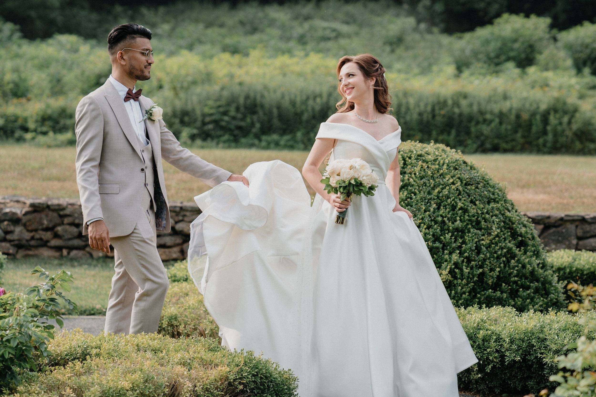 Wedding couple in garden setting with bride's dress flowing in the wind.