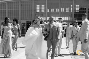 Black and white wedding photo of bride and groom with bridal party outside a large venue building.
