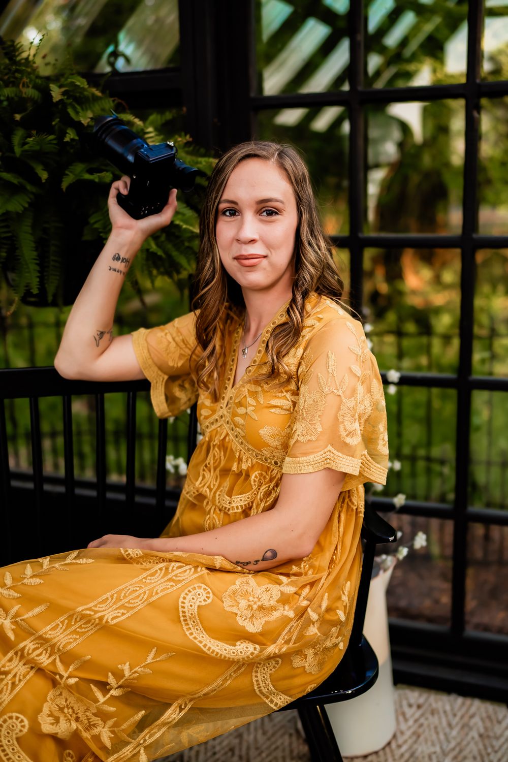 Woman in yellow floral dress poses with camera equipment during golden hour photoshoot.