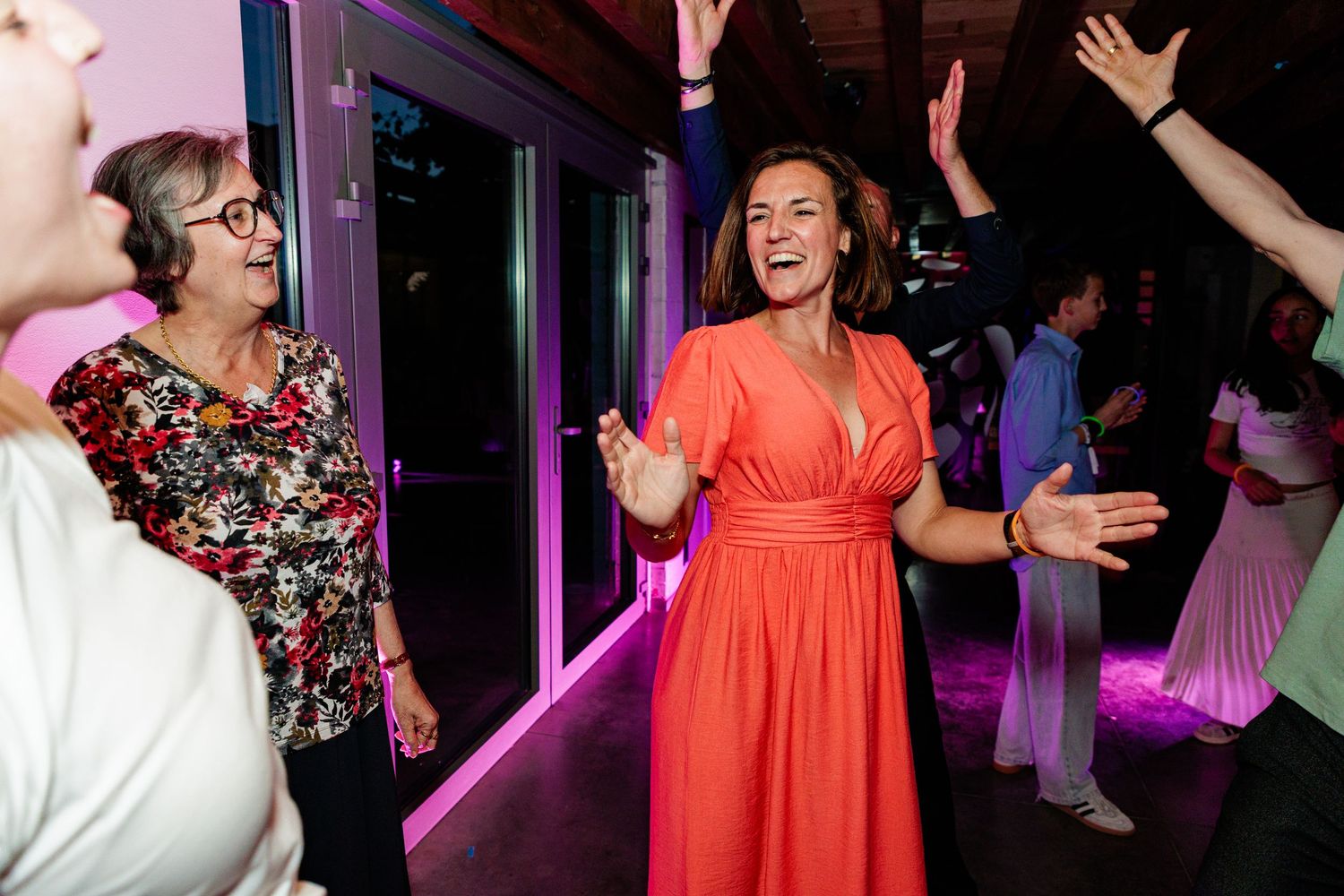 Dancers in colorful dresses party on a dance floor illuminated by purple lights at a celebration event.