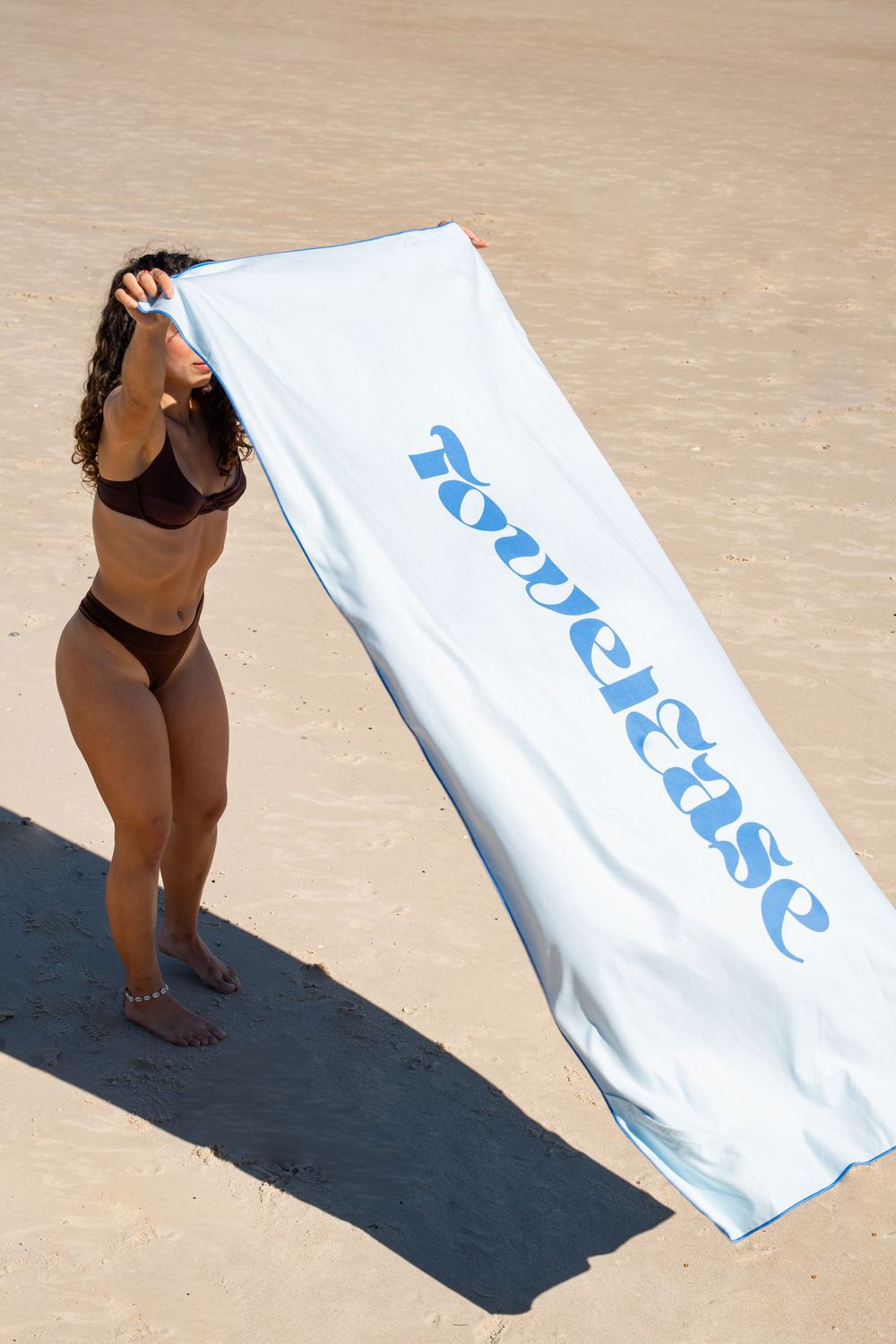 A sequence of images showing a beach towel being laid out on a dark mat against a beige background.