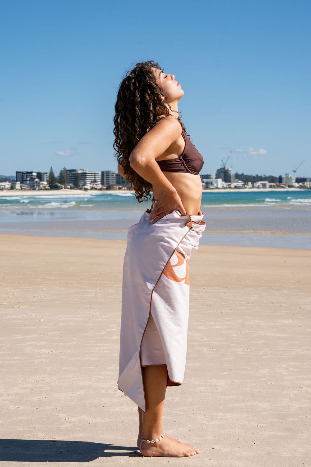 Person doing yoga exercises on a beautiful sandy beach with city skyline in background.