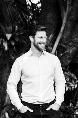 Black and white outdoor portrait against tropical foliage wearing a crisp white shirt.