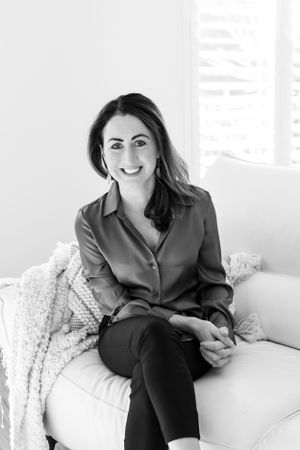 Professional portrait of someone sitting casually on a white couch wearing a dark button-down shirt.