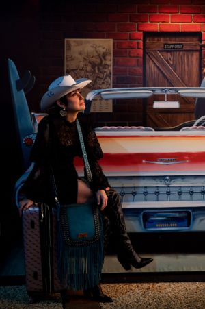 A western-styled shoot against a brick wall with a vintage car featuring cowboy boots and fringe accessories.