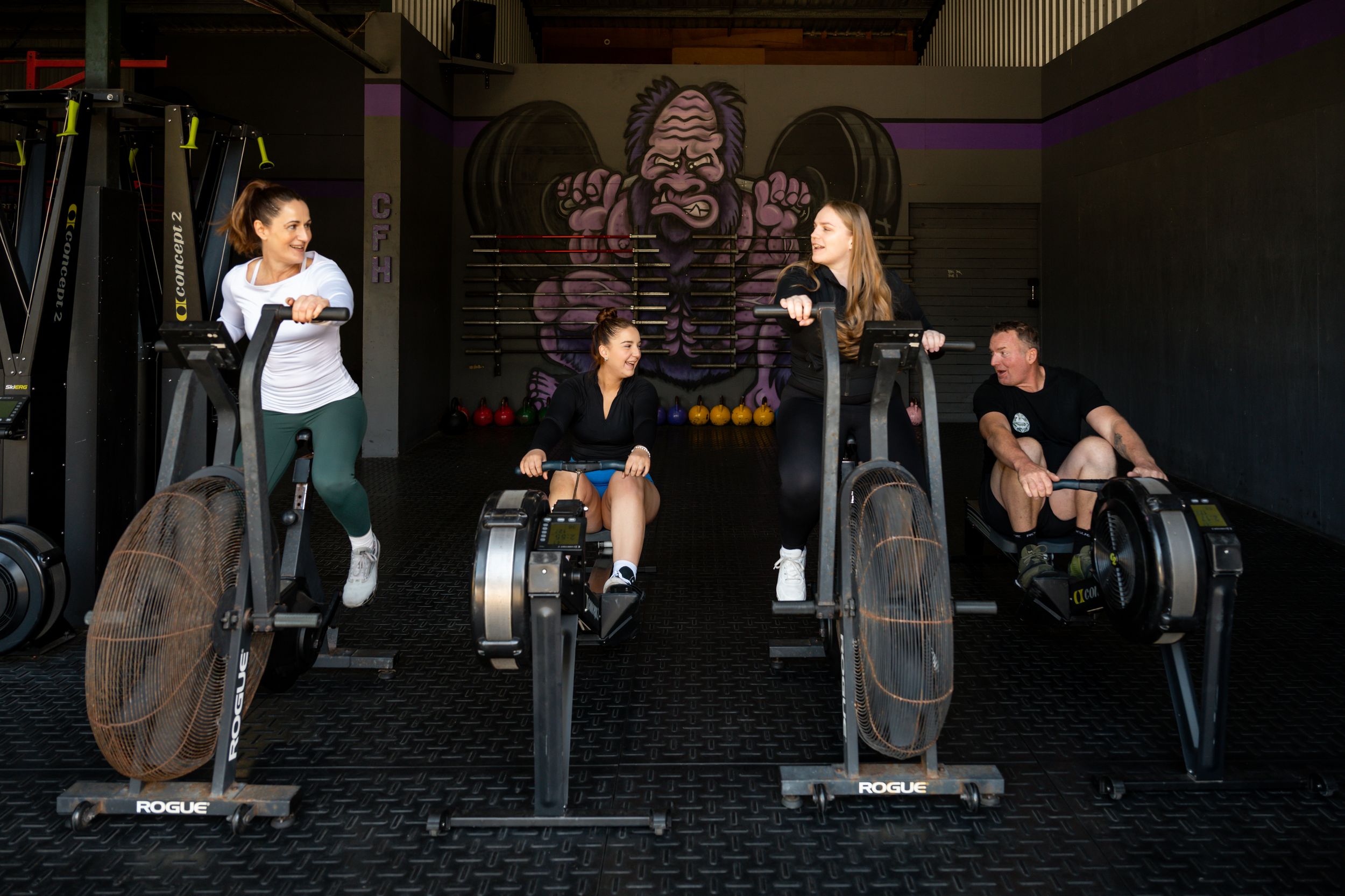 Athletes performing weighted squats and exercises in a dark CrossFit-style gym with industrial lighting.