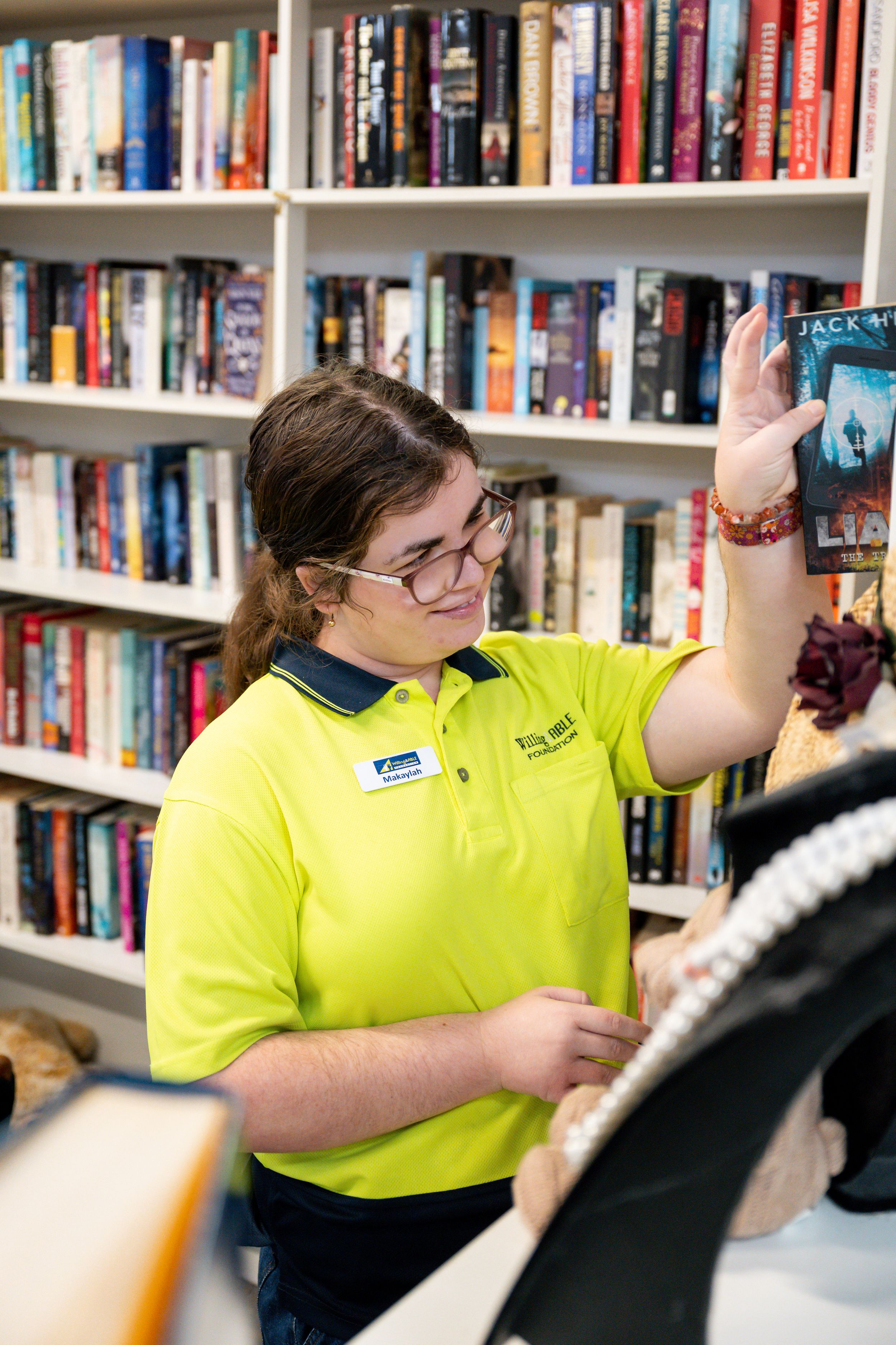 A staff member in a yellow polo shirt helps customers in a bookstore with shelves of books in the background.
