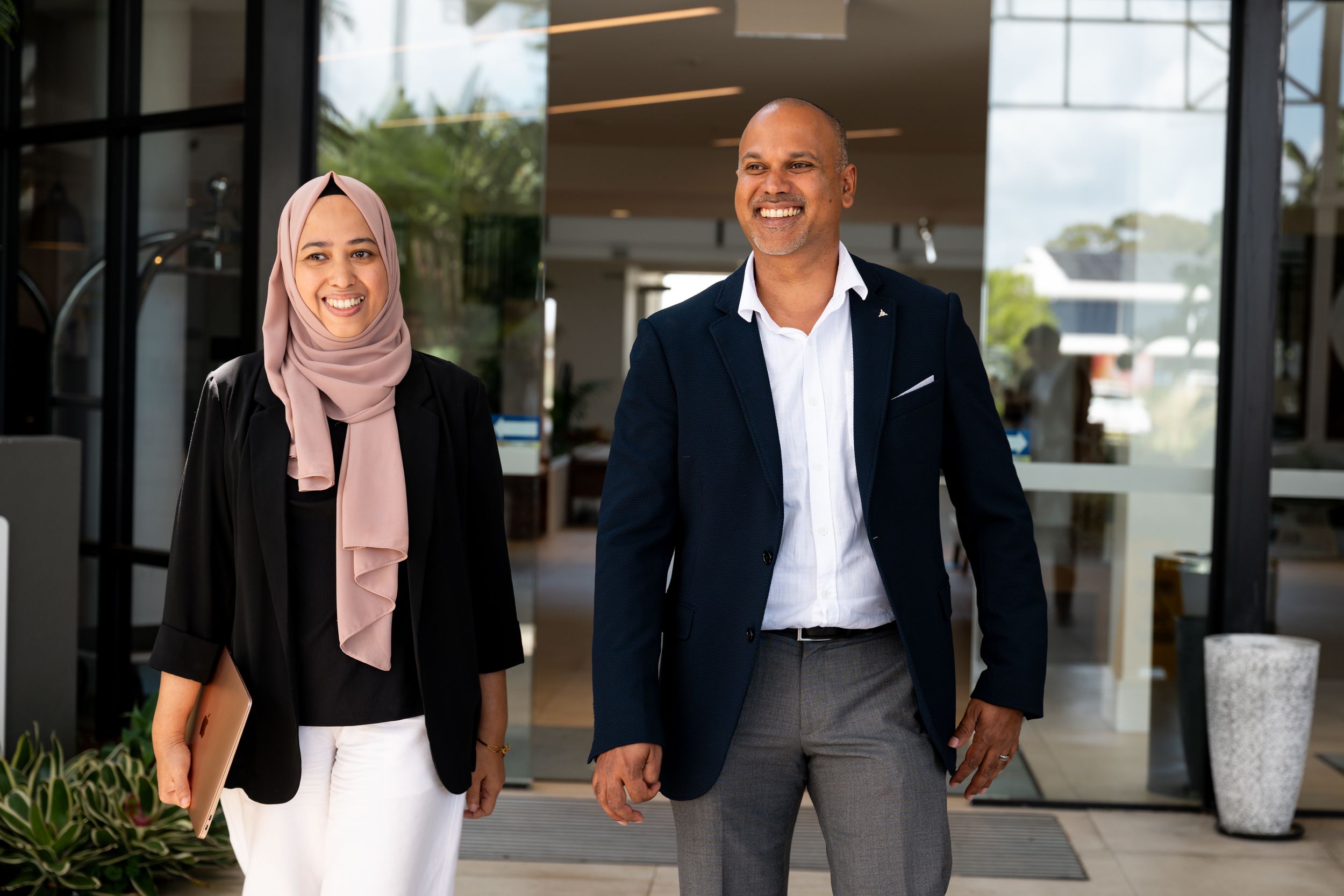 Business professionals in formal attire walk through a modern office building lobby.