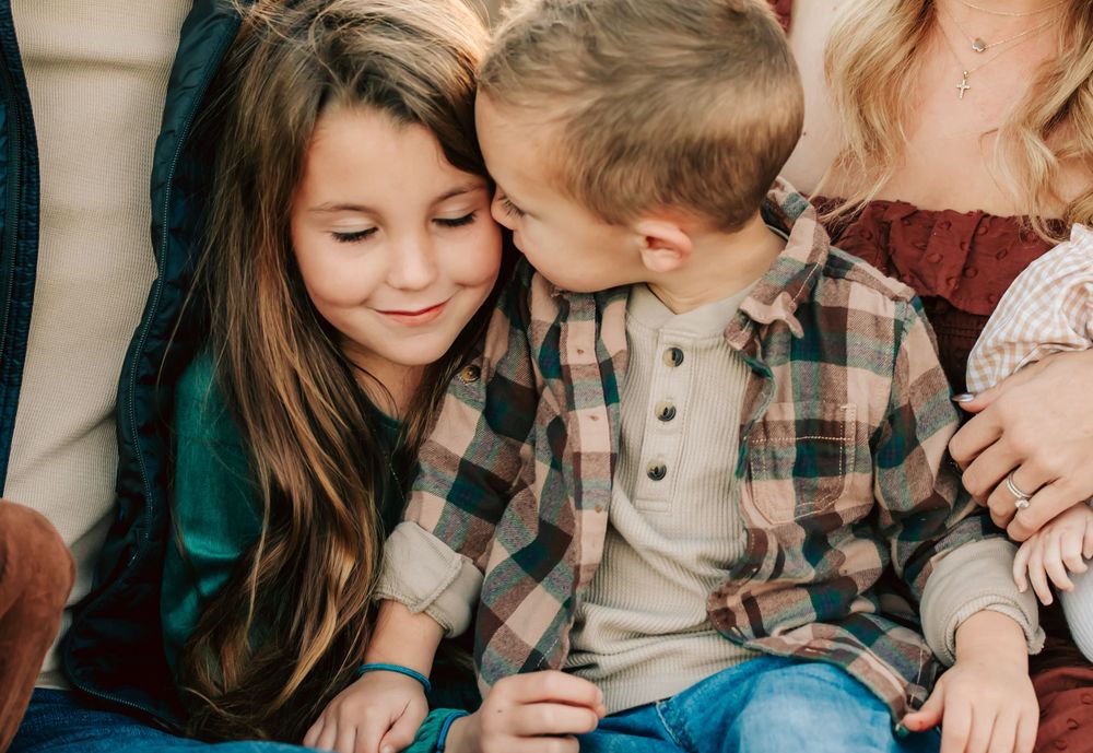 Two young children share a sweet moment together wearing casual autumn clothing on a couch.