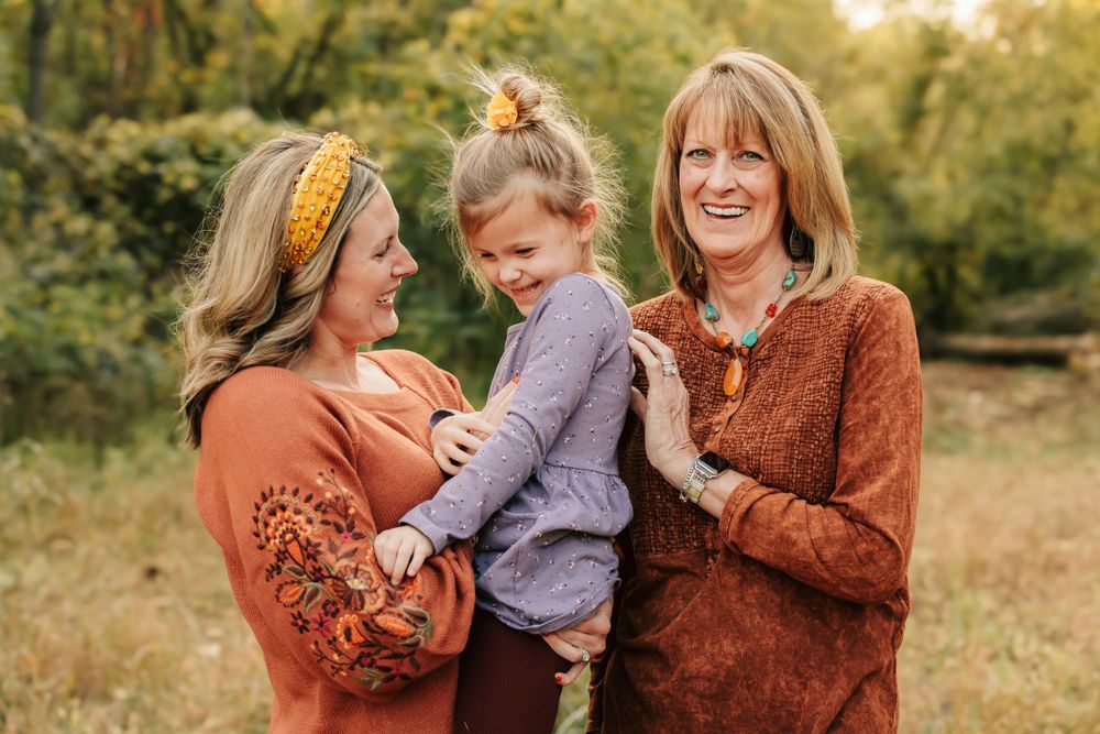 Three generations wearing cozy autumn sweaters share a joyful moment together outdoors during golden hour.